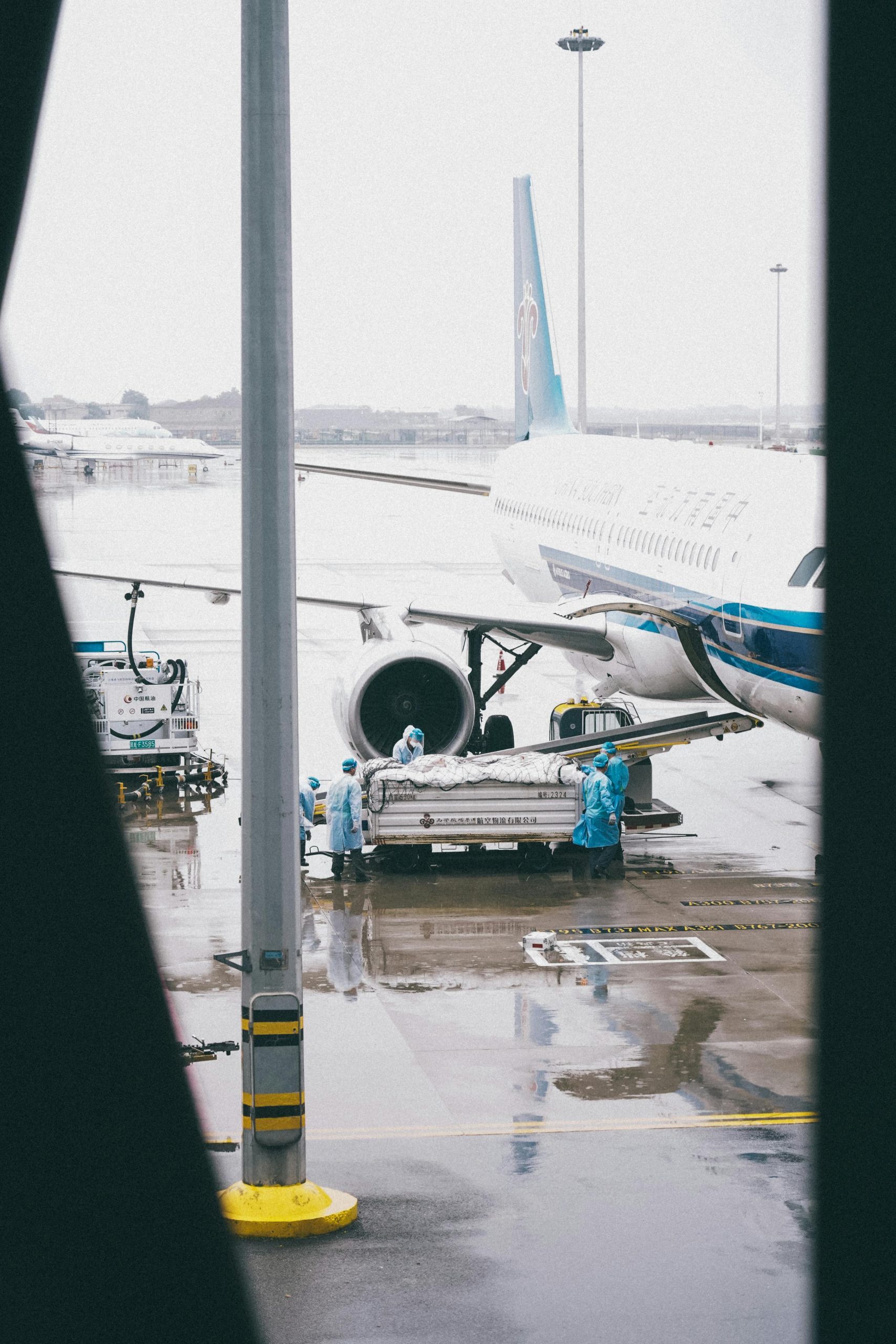 Workers in protective gear load cargo onto an airplane at Shanghai airport.