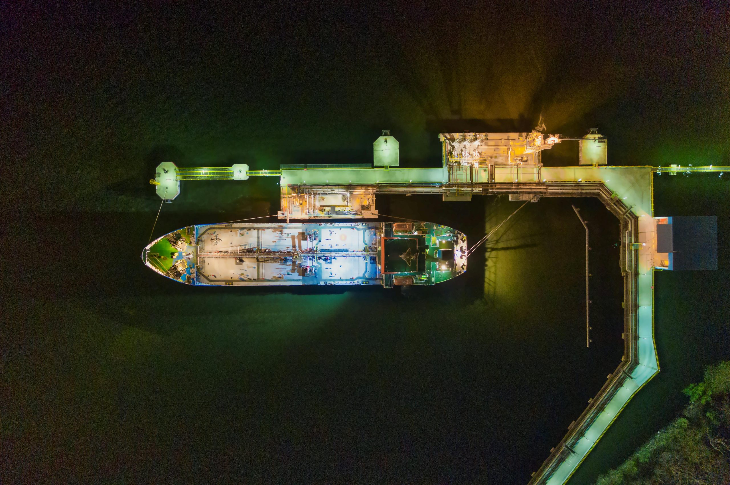 An aerial view of a cargo ship docked at a brightly illuminated pier during nighttime.